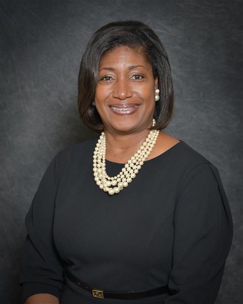 Yoluanda Daniel's professional headshot; wearing a black dress against a grey background