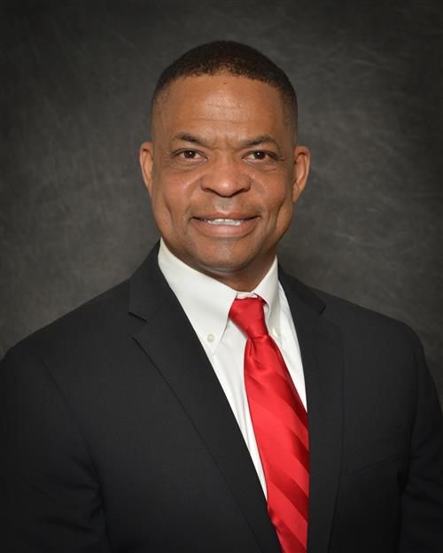 Elliot Patrick's professional headshot; wearing a black suit and red tieagainst a grey background