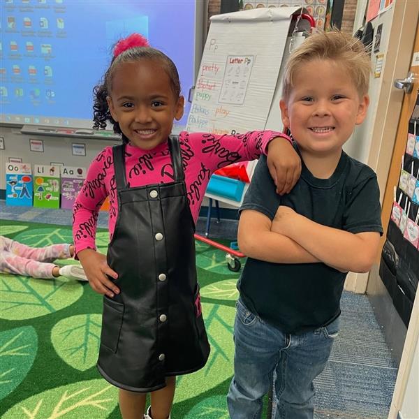  Two smiling children standing together in a classroom.