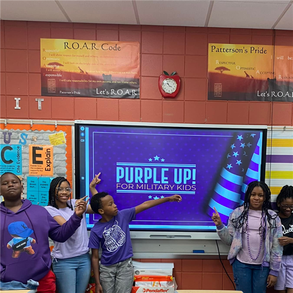  A group of six students standing in front of a digital screen that displays 'Purple Up! For Militar