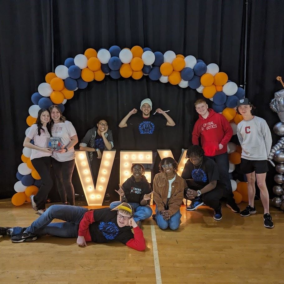  A group of exuberant students and their teacher pose for a photo at a VEX Robotics event. Two girls